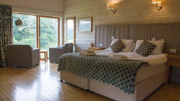 Un dormitorio con una cama grande, dos mesitas de noche, una silla y vistas al exterior a través de una ventana.