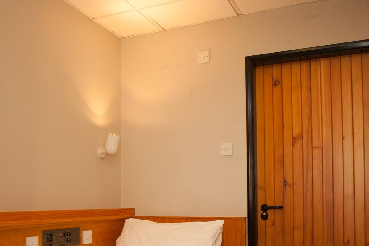 Ein Hotelzimmer mit einem Einzelbett, einer Holztür und einer wandmontierten Lampe.