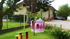 Ein Spielplatz mit Rutsche, einem kleinen Haus und einem in der Nähe stehenden Auto.