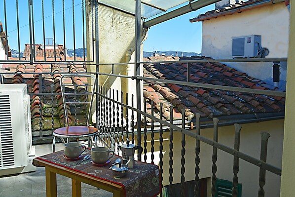 A balcony with a table, chairs, and a view of terracotta-roofed buildings. - Colonna Apartment with Terrace (Florence)