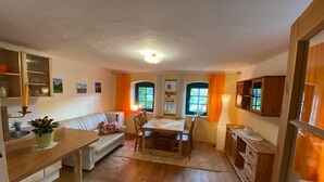 A cozy kitchen and dining area with wooden floors, a white sofa, a dining table with chairs, and a small kitchen counter with a plant. - Grüne Idylle im Dresdener Süden (Bannewitz)
