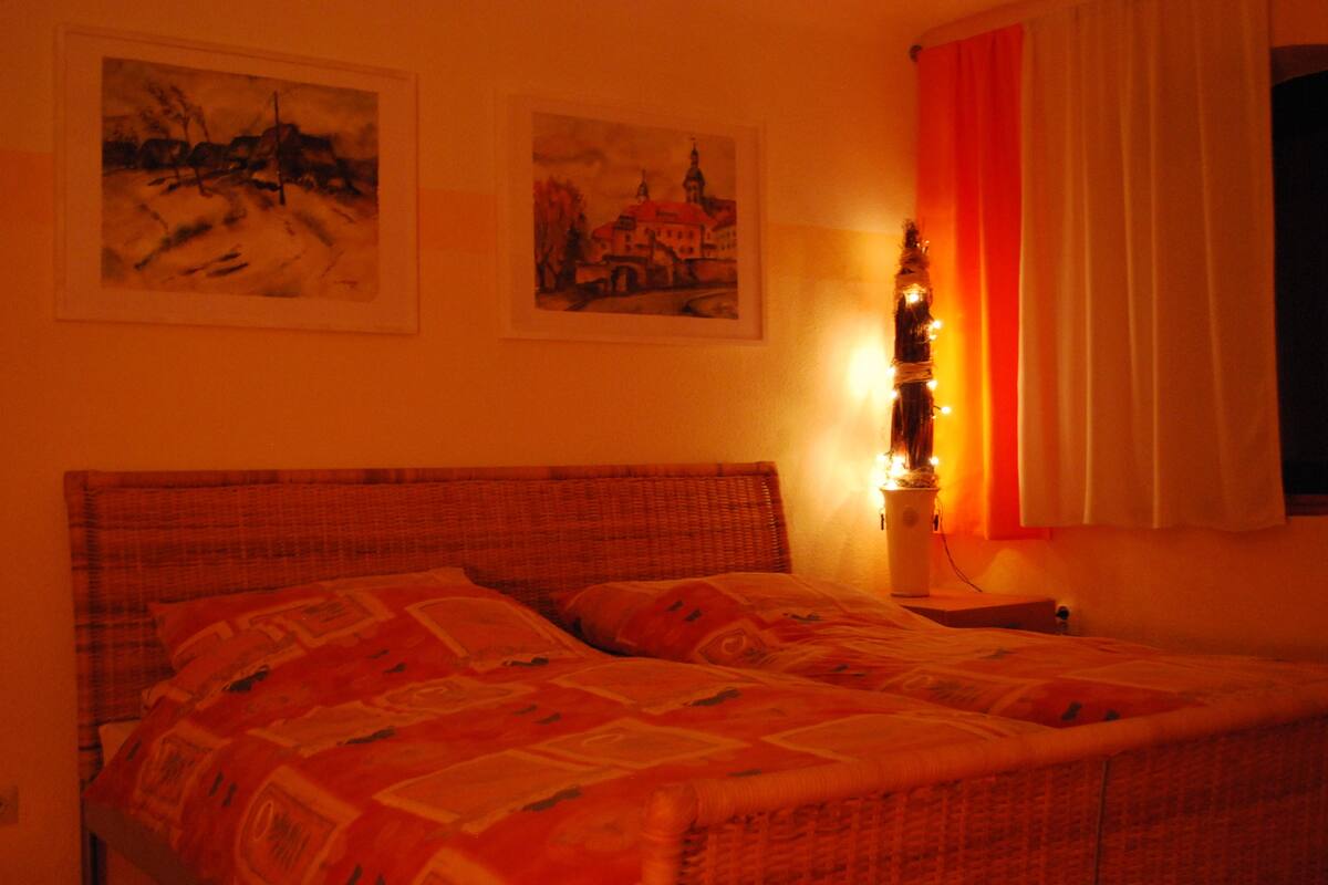 A bed with a patterned bedspread, a nightstand with a lamp, and two framed pictures on the wall.