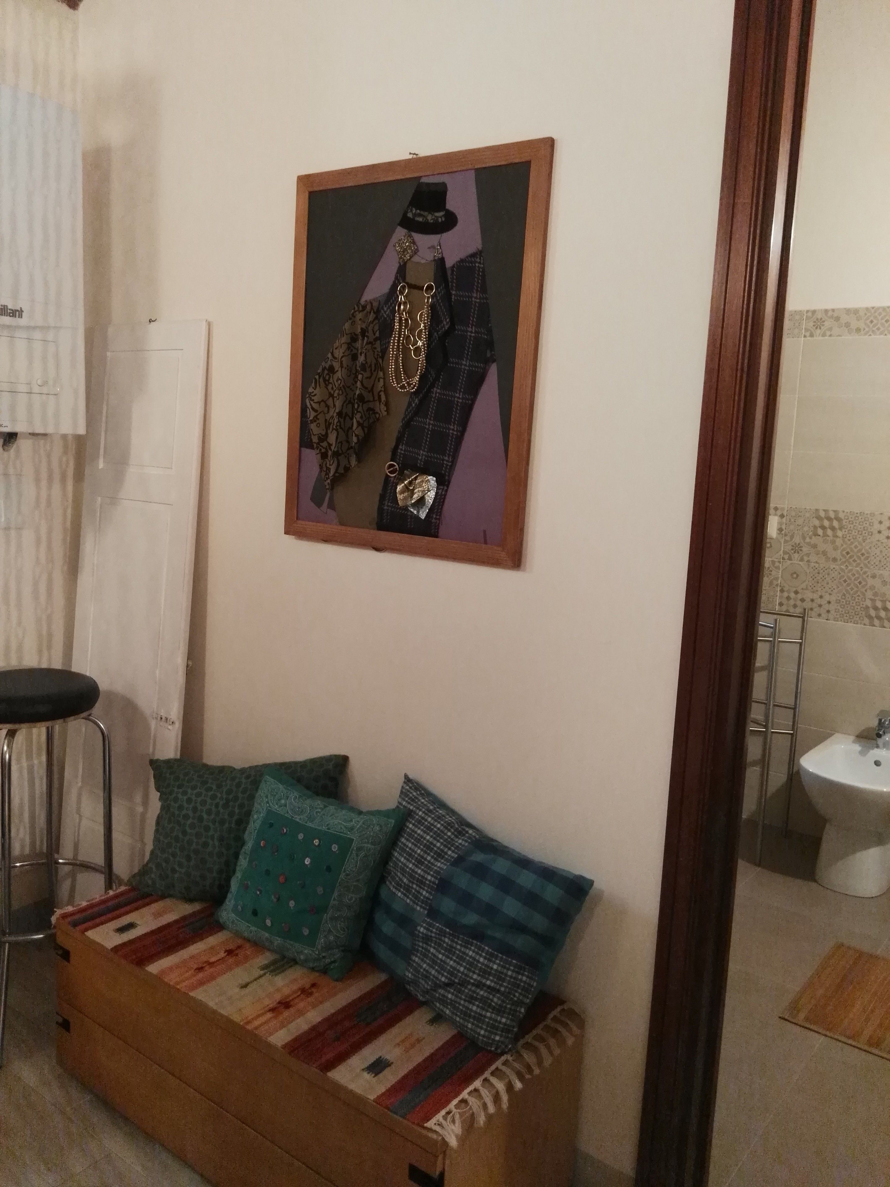 Ein Zimmer mit einer Couch, einem gerahmten Bild an der Wand, einem Barhocker und einem durch eine Glastür einsehbaren Badezimmer.