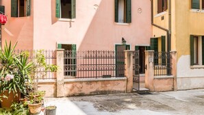 Ein pinkfarbenes Gebäude mit grünen Fensterläden, einem verschlossenen Eingang und Topfpflanzen im Vordergrund.