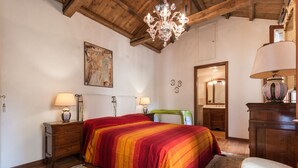 Ein Schlafzimmer mit einem großen Bett, einem Holz-Kopfende, zwei Nachttischen mit Lampen, einer Pendelleuchte, einem Bild an der Wand und einem Spiegel im Hintergrund.