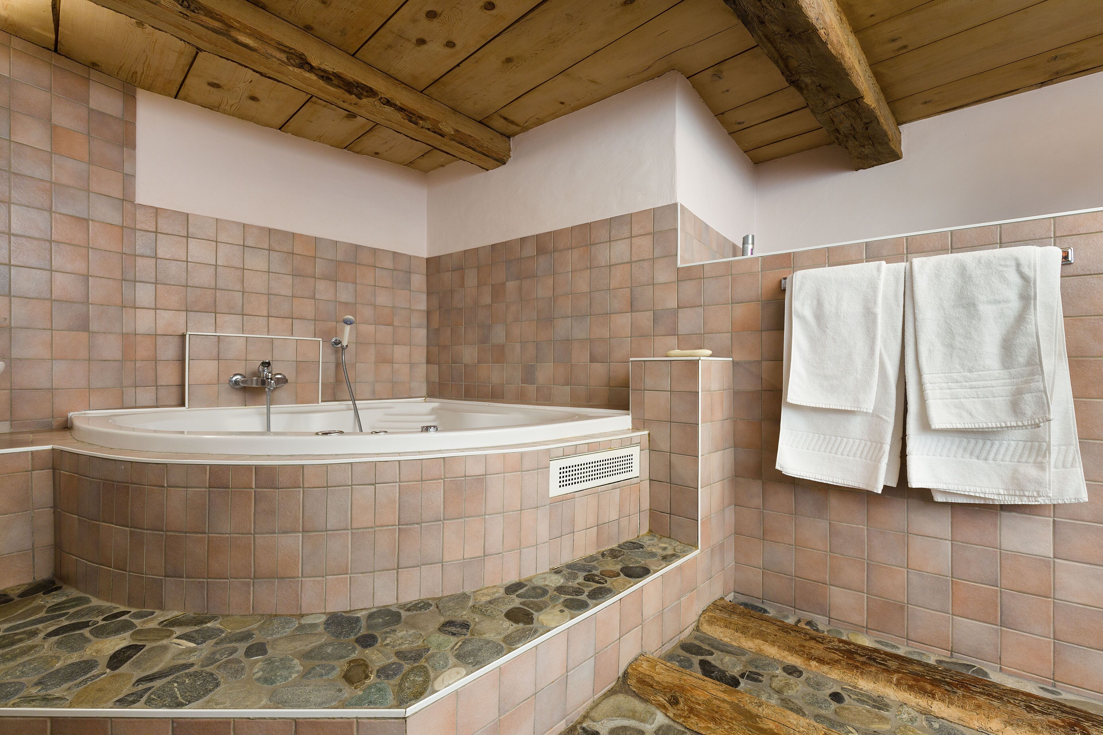 Un baño con suelo de baldosas de piedra, una bañera independiente y un perchero con toallas.