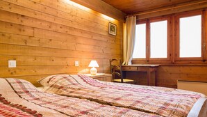 Une pièce aux murs lambrissés, comprenant un lit, une table de chevet avec une lampe, une chaise et une fenêtre avec des rideaux.