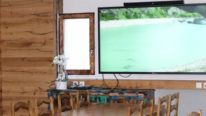Une table à manger en bois avec des chaises, un téléviseur fixé au mur et un miroir encadré.