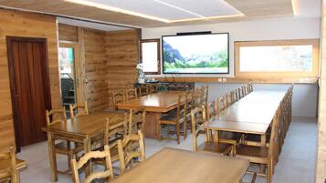 A long wooden dining table with chairs, a television mounted on the wall, and a window with a mountain view.