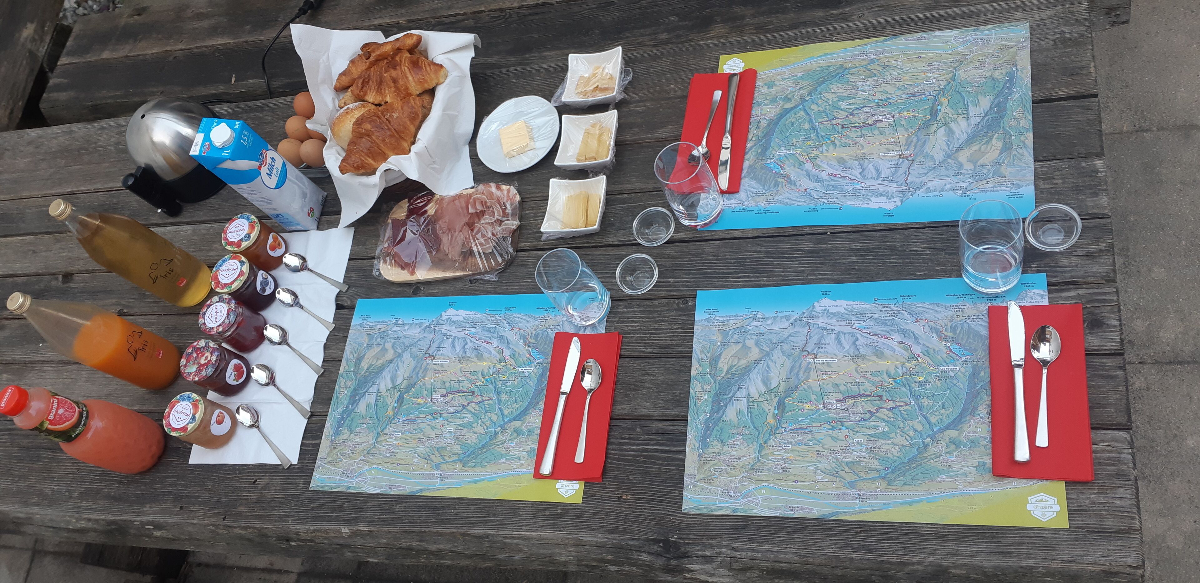 A picnic setup on a wooden table with a map, food items, and drinks.