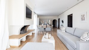 Un salon moderne avec une cheminée, un canapé, un coin repas et une cuisine en arrière-plan.