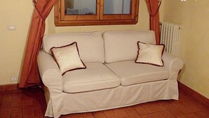 Ein beiges Sofa mit zwei Kissen, ein Fenster mit Vorhängen und eine Heizung.