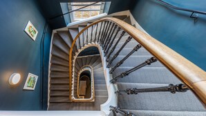 A spiral staircase with a wooden handrail and metal balusters, leading to a landing with a small mirror and framed pictures on the walls. - No1. Apartments Edinburgh - George IV Bridge (Edinburgh)