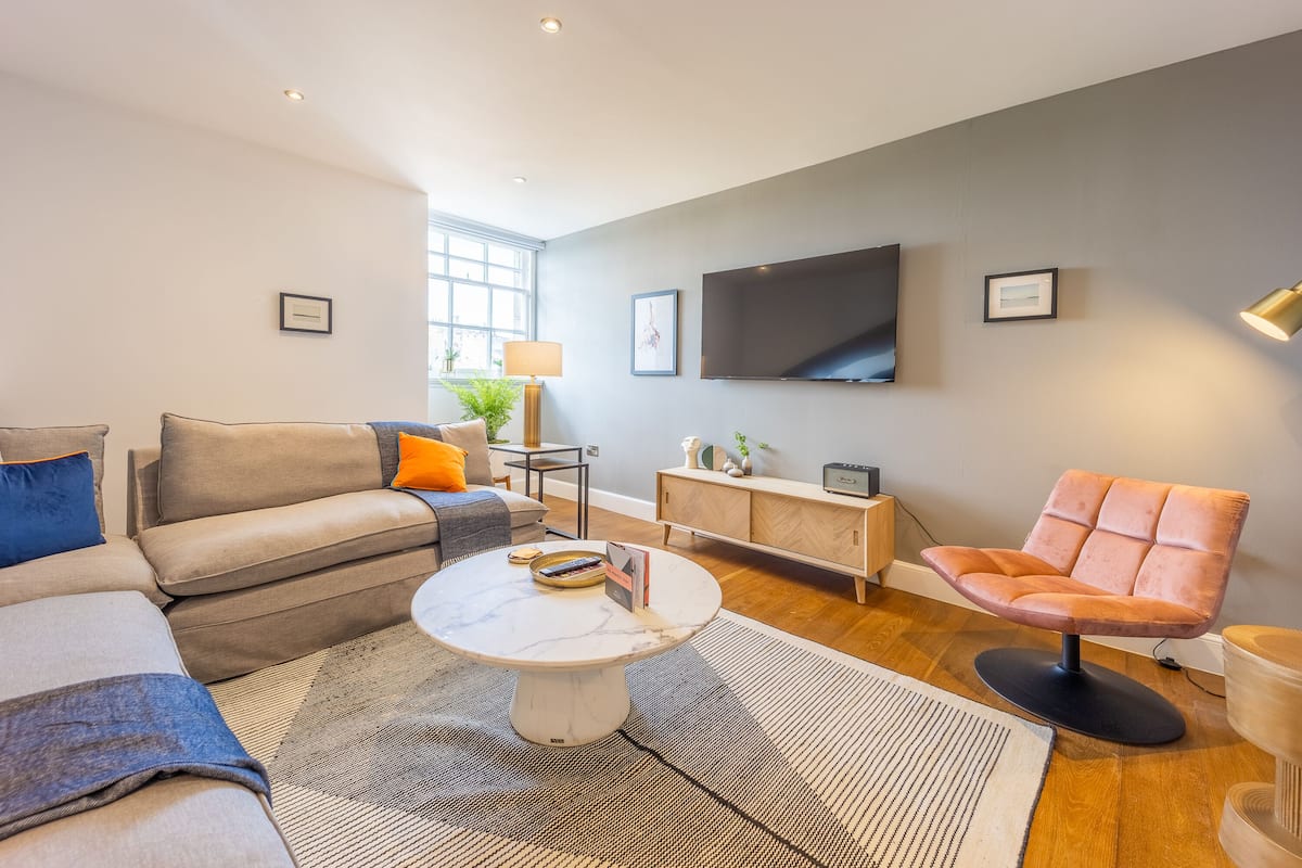 A modern living room with a sofa, armchair, coffee table, and a flat-screen TV mounted on the wall.