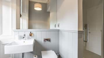 Une salle de bain avec un lavabo, des toilettes et une douche, le tout de couleur blanche.