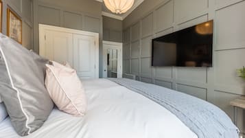 A bedroom with a large bed, a television mounted on the wall, and a door leading to another room.