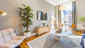 A modern living room with a sofa, a dining table, and a large potted plant. - No1. Apartments Edinburgh - George IV Bridge (Edinburgh)