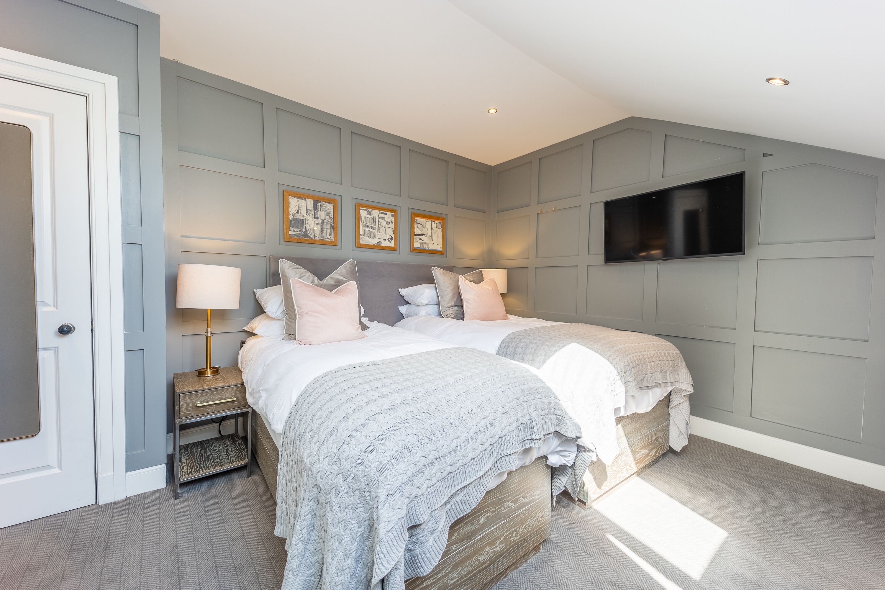A bedroom with two beds, a TV mounted on the wall, and a nightstand with a lamp.