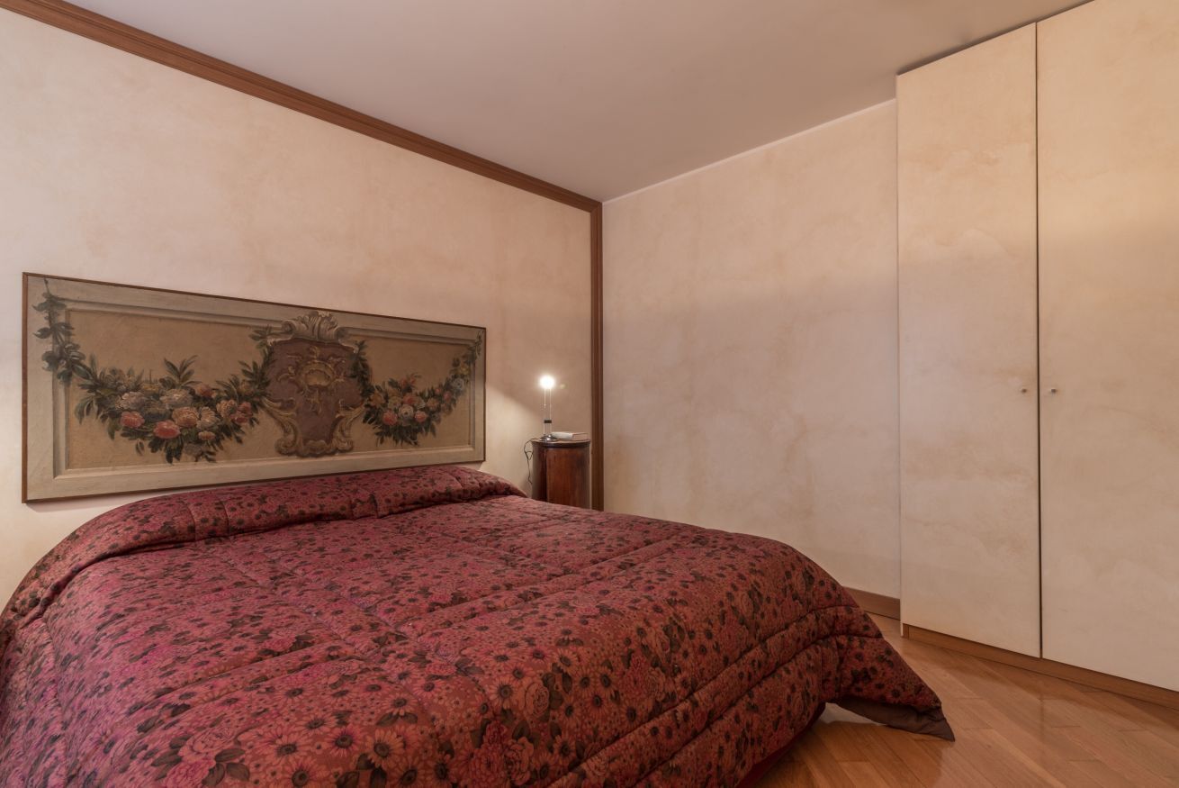 A bedroom with a bed, a nightstand, a wall-mounted lamp, and a wardrobe.