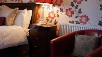 A bedroom with a bed, a nightstand, a red chair, and a wall with floral wallpaper.