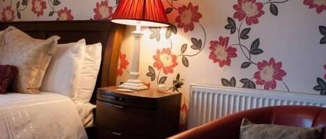 A bedroom with a bed, a nightstand, a red chair, and a wall with floral wallpaper.