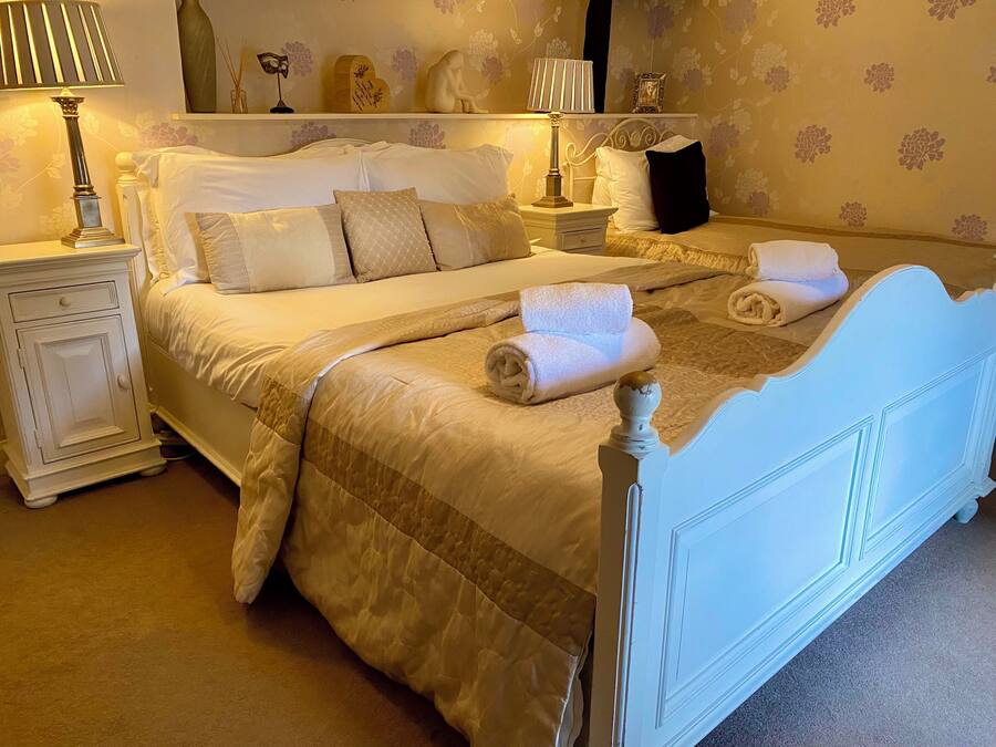 A neatly made bed with a quilted cover, two bedside tables with lamps, and a wall with floral wallpaper.