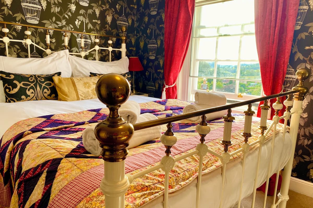 Un lit avec un cadre blanc, une courtepointe aux couleurs vives et une tête de lit en bois ornée d’un élément décoratif.