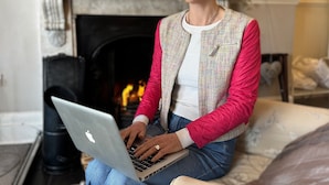 A person sitting on a bed using a laptop in a room with a fireplace.
