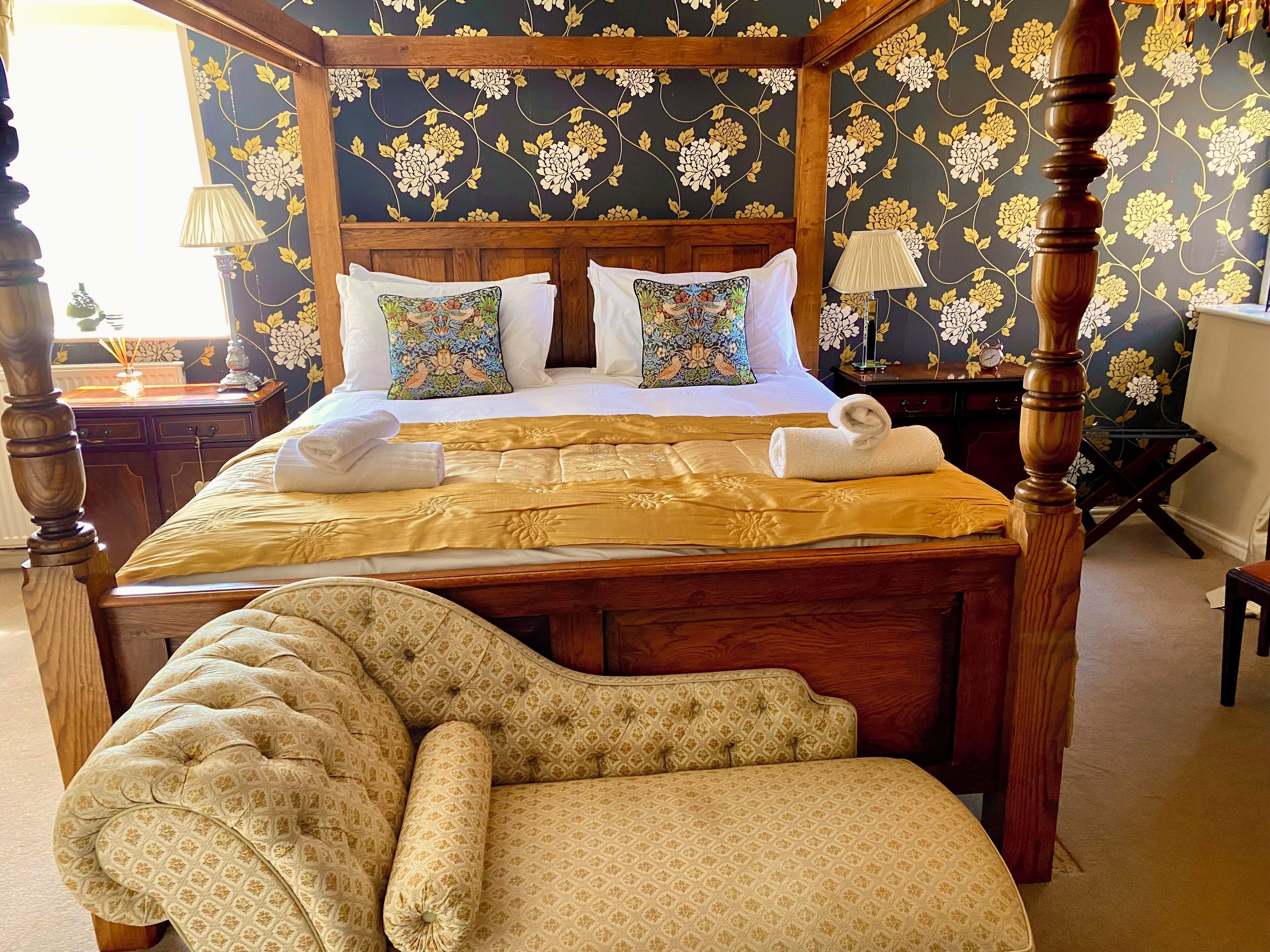 A four-poster bed with a gold bedspread, two decorative pillows, and a matching upholstered bench.