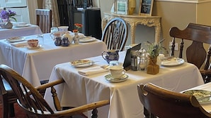 A dining area with tables set for tea service, featuring floral-patterned tableware and vintage chairs.