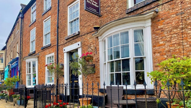 A brick building with a large arched window, a black metal fence, and potted plants.