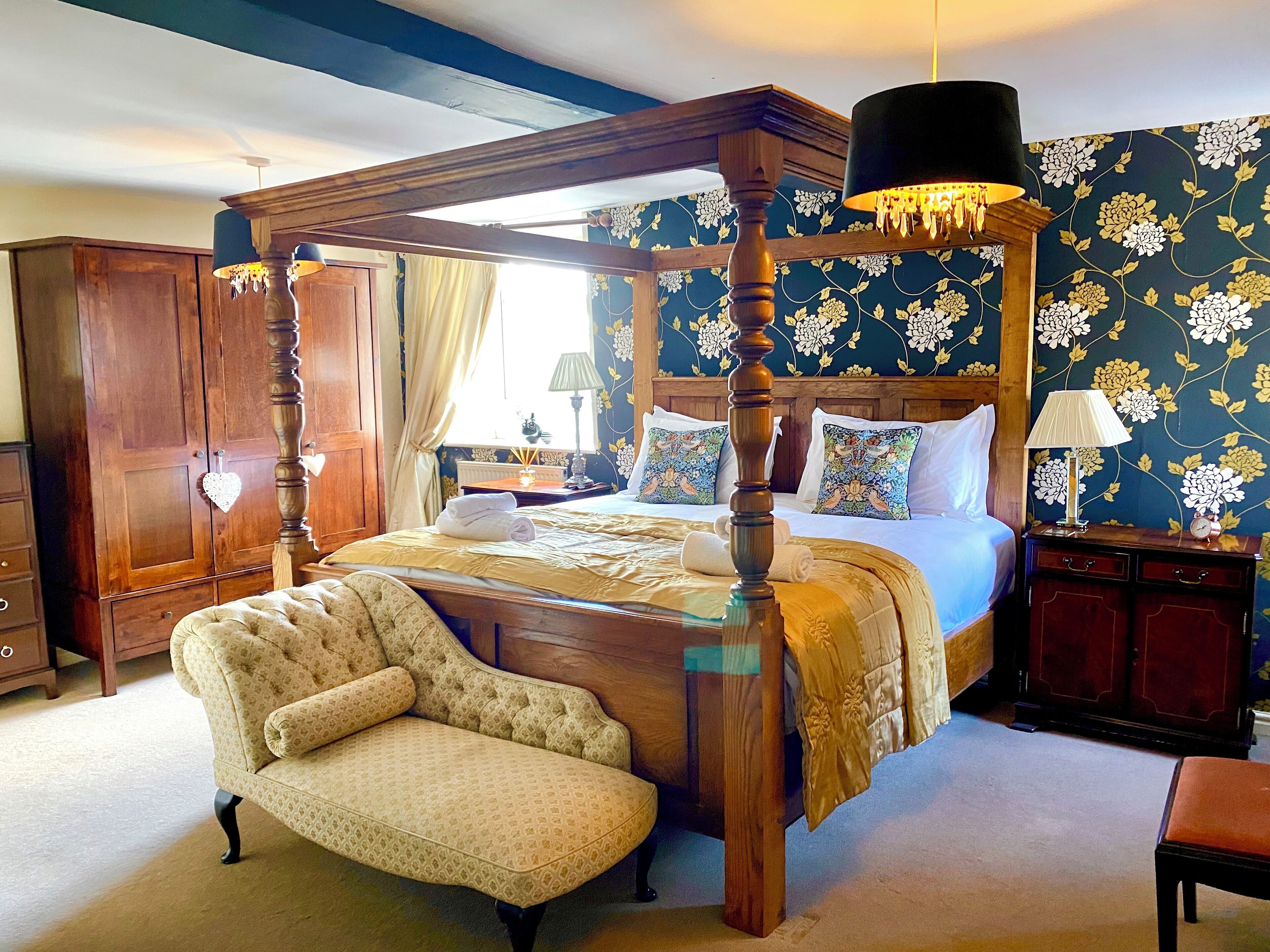 A four-poster bed with a canopy, a tufted armchair, and a nightstand with a lamp.