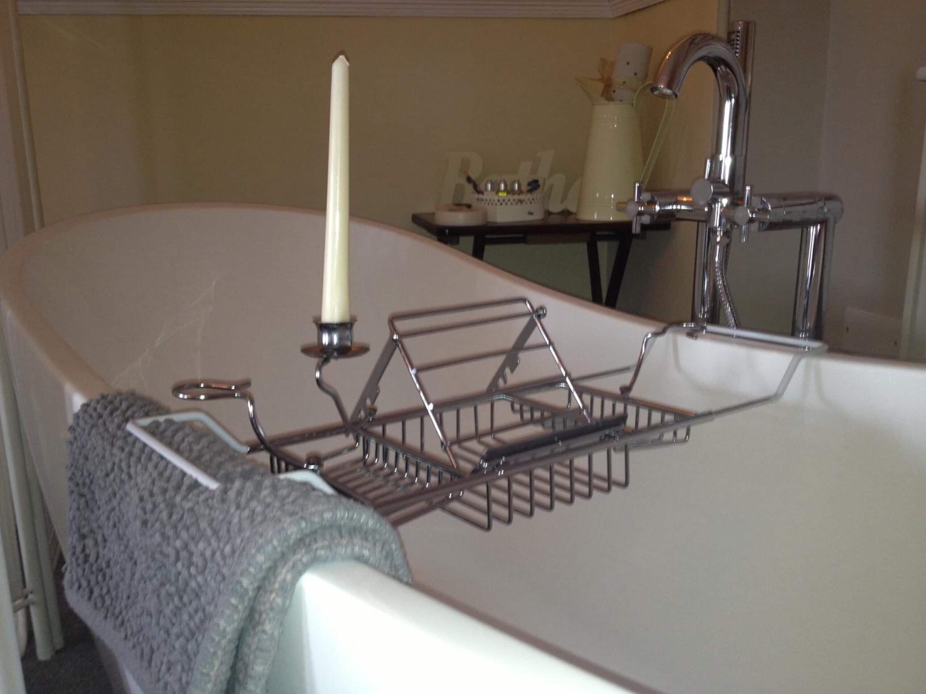 Ein Badezimmer mit einer Badewanne, einem Metallregal, einer Kerze und einem Handtuch.