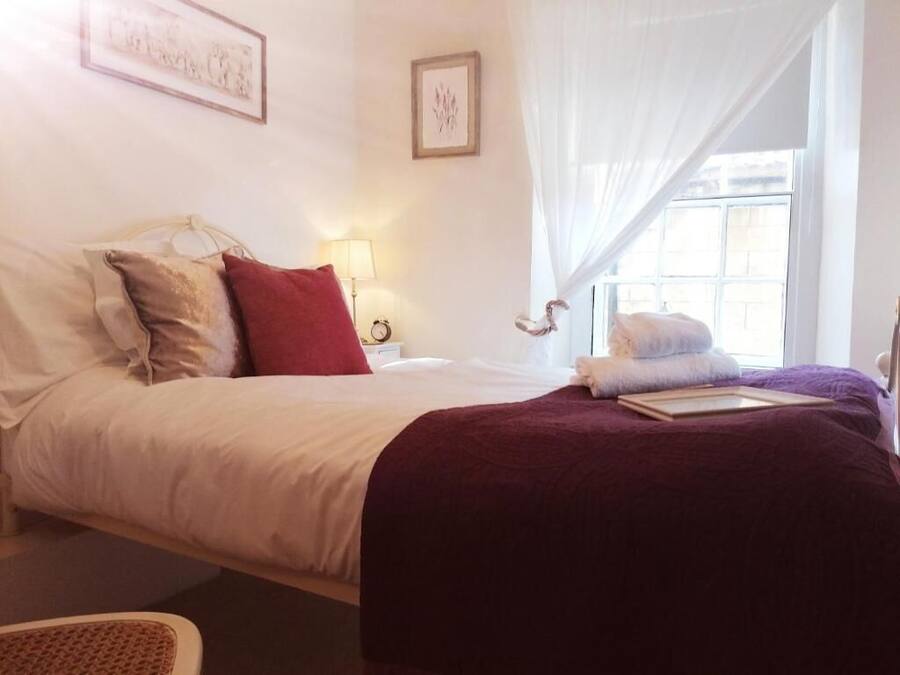 A neatly made bed with white and red pillows, a purple blanket, and a bedside lamp.