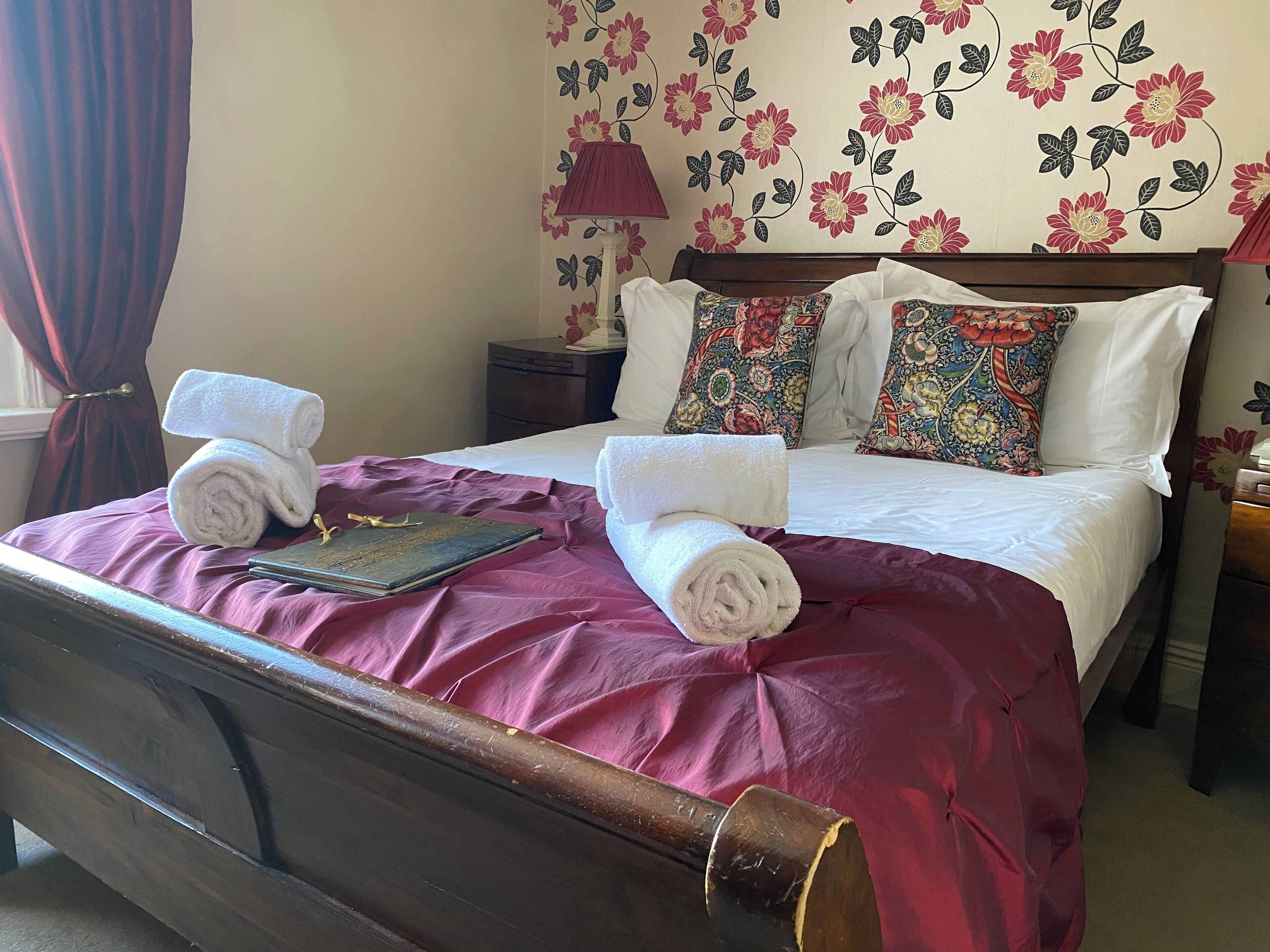 A neatly made bed with a purple bedspread, two rolled white towels, and a book on the bed.
