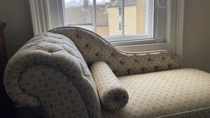 A corner sofa with a patterned fabric and a window with a view of buildings.