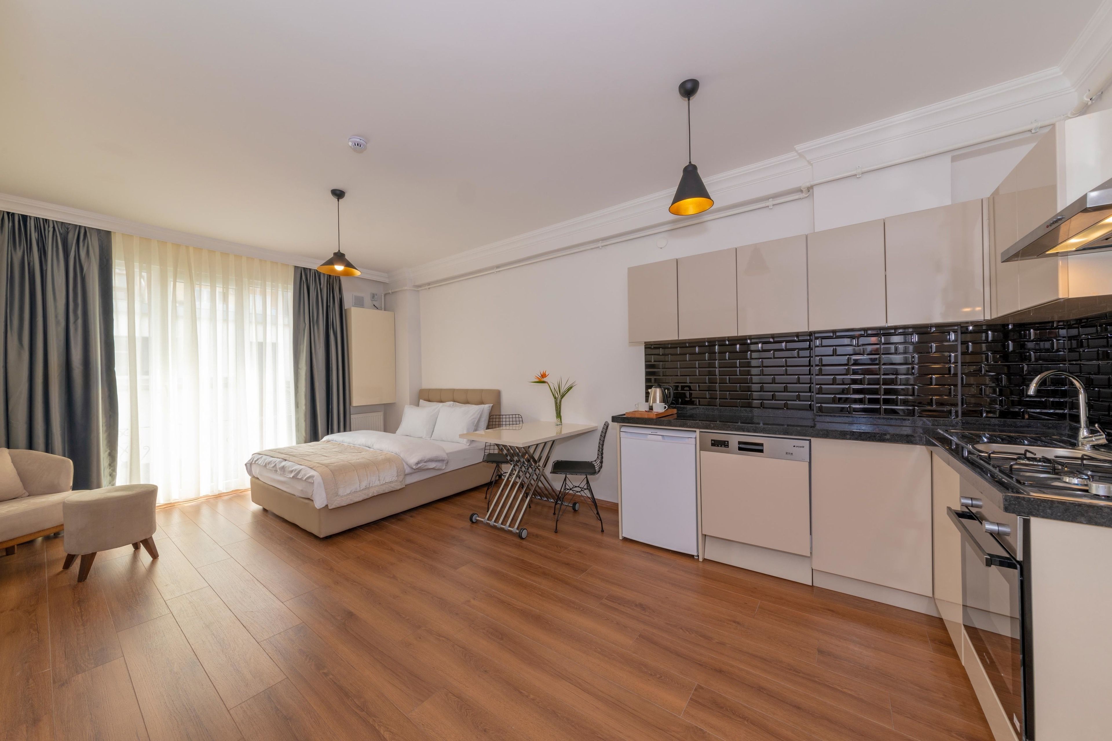 A modern hotel room with a bed, bedside table, and a small kitchenette.