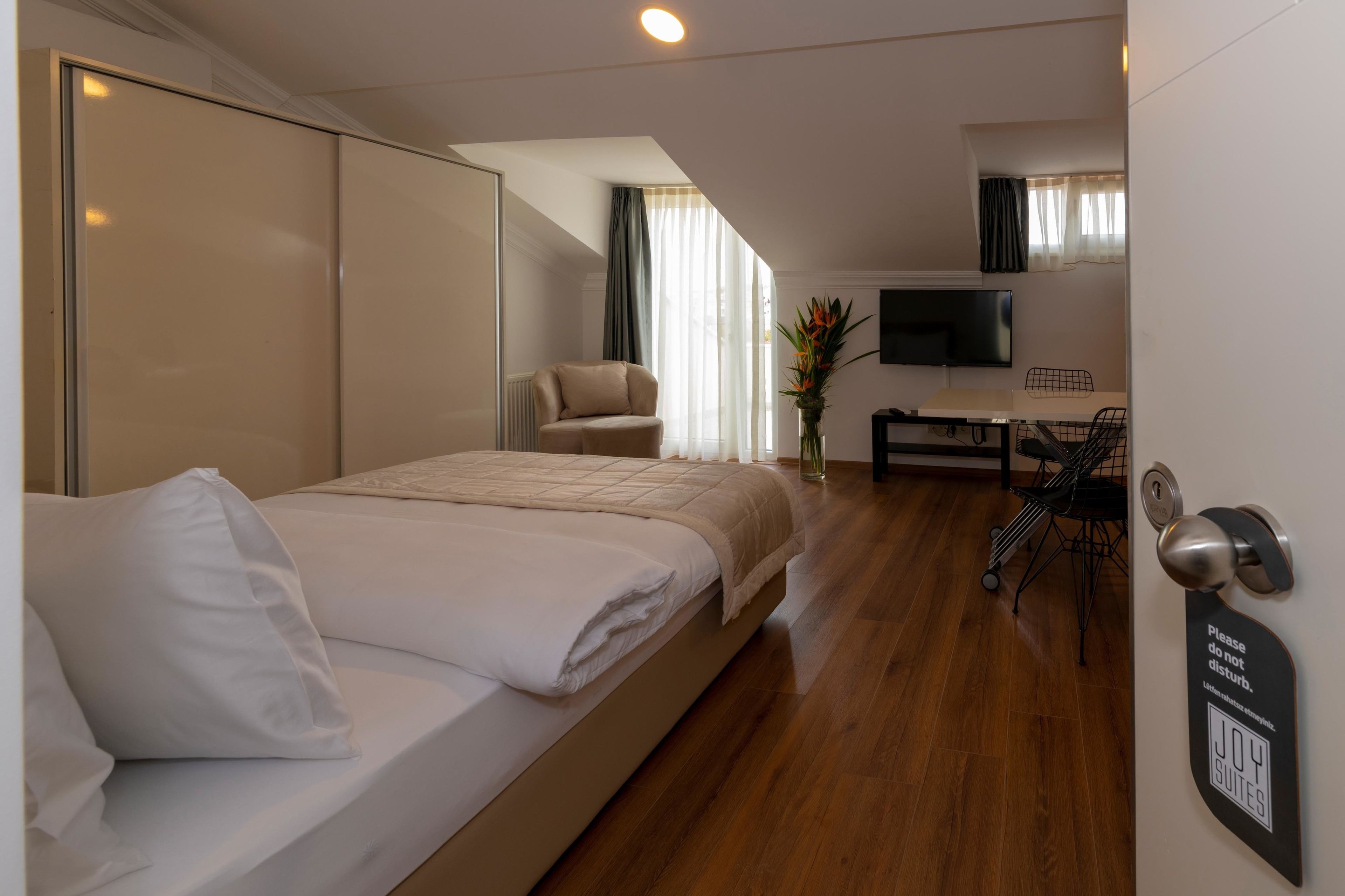 A hotel room with a bed, a desk, a chair, a TV, and a door with a sign.
