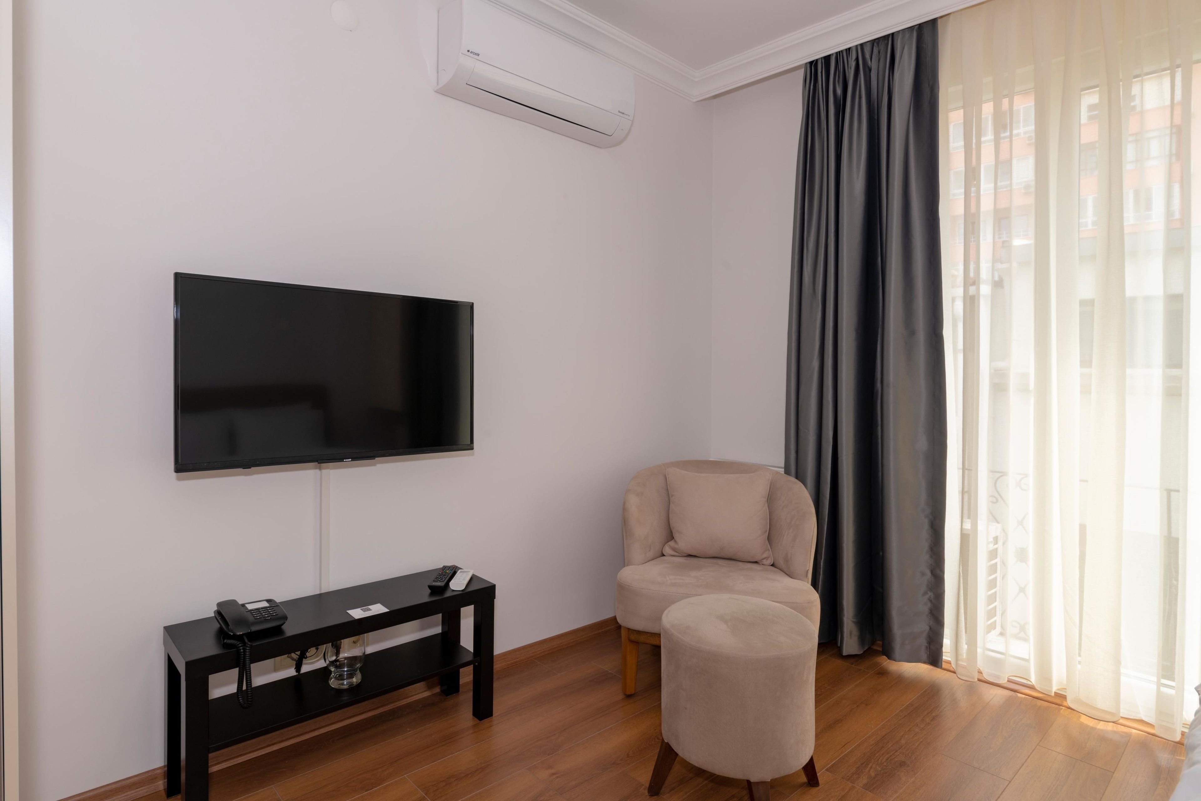 Una sala de estar moderna con un televisor de pantalla plana, una consola negra con un teléfono, un sillón beige y un pequeño otoman.