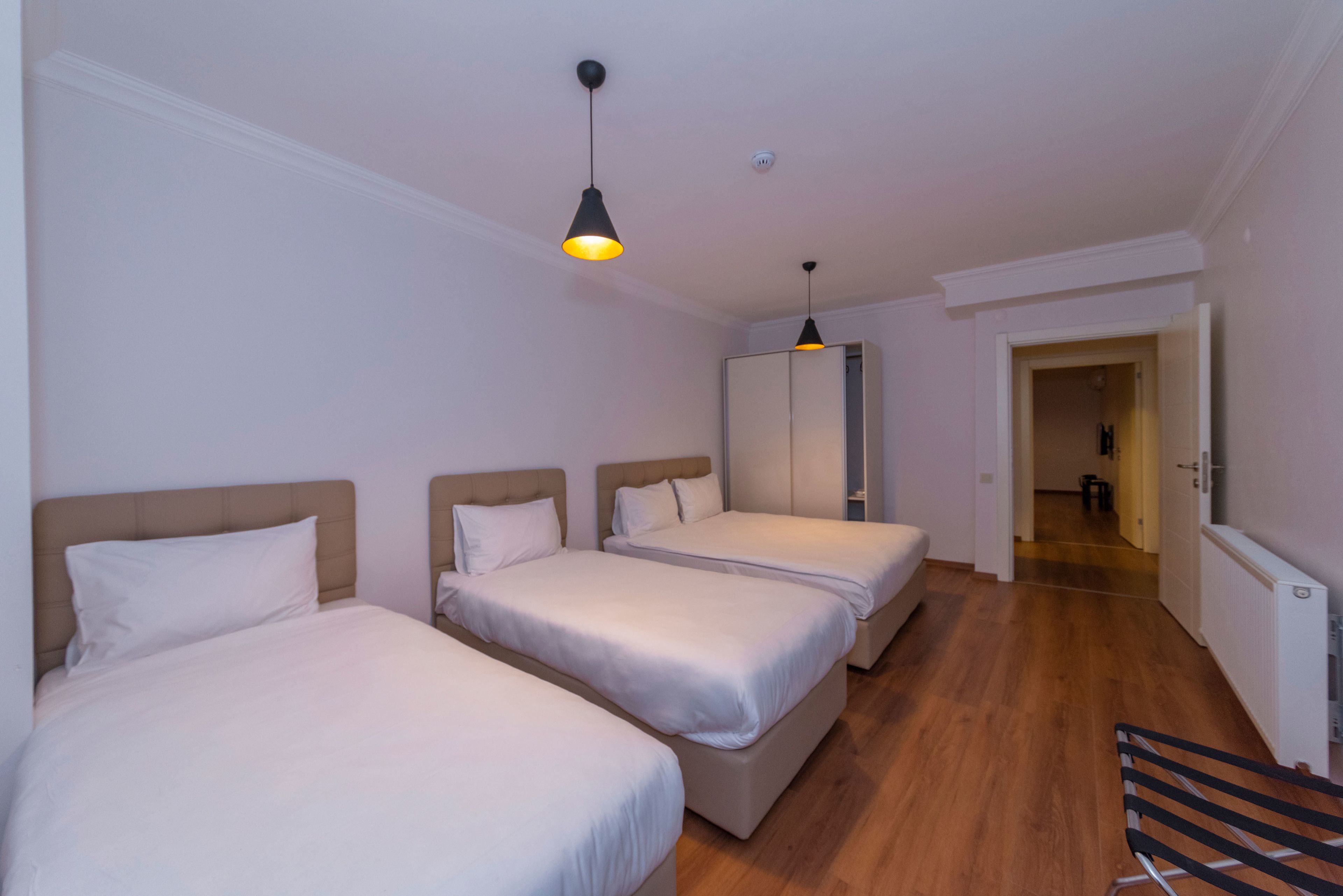 A hotel room with three beds, a wooden floor, and a hallway leading to another room.
