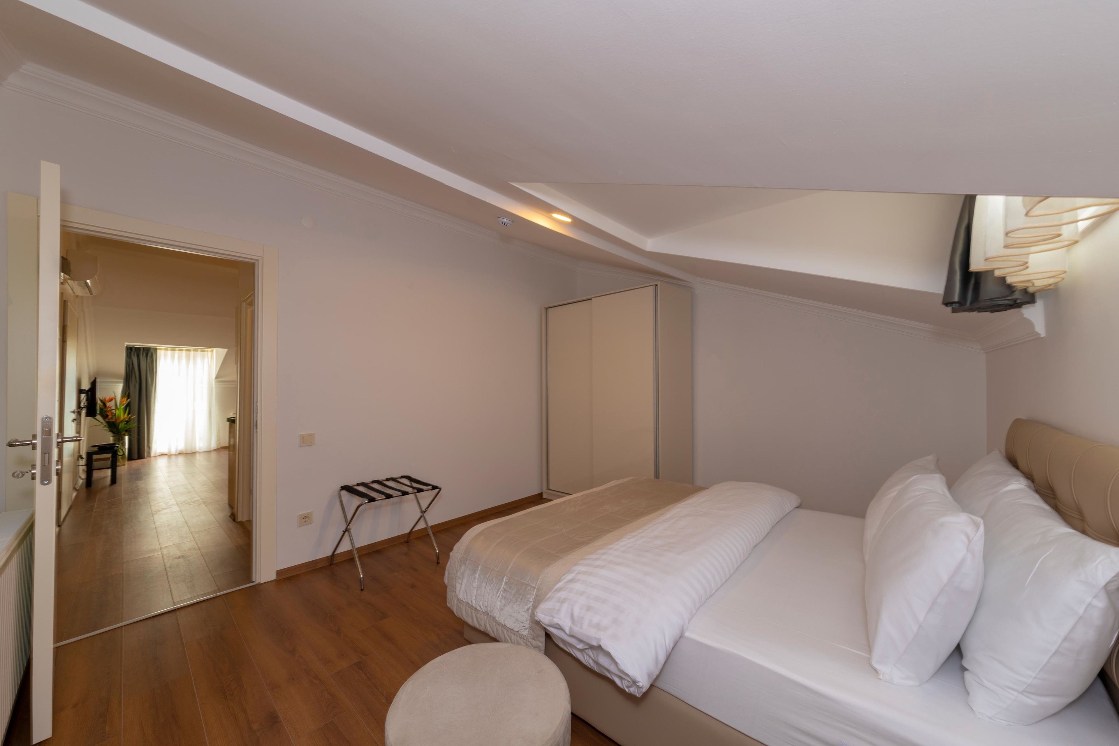 Een slaapkamer met een bed, een klein krukje en een spiegel.