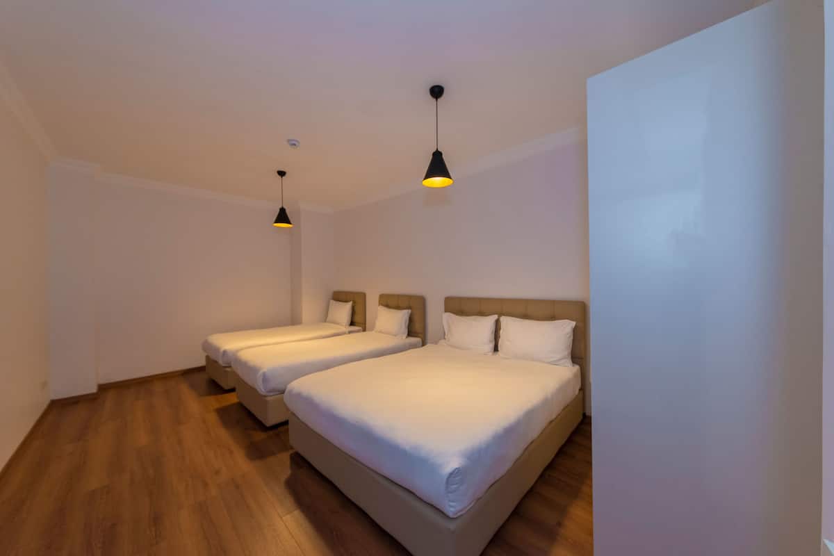 A hotel room with two single beds, wooden flooring, and pendant lighting.