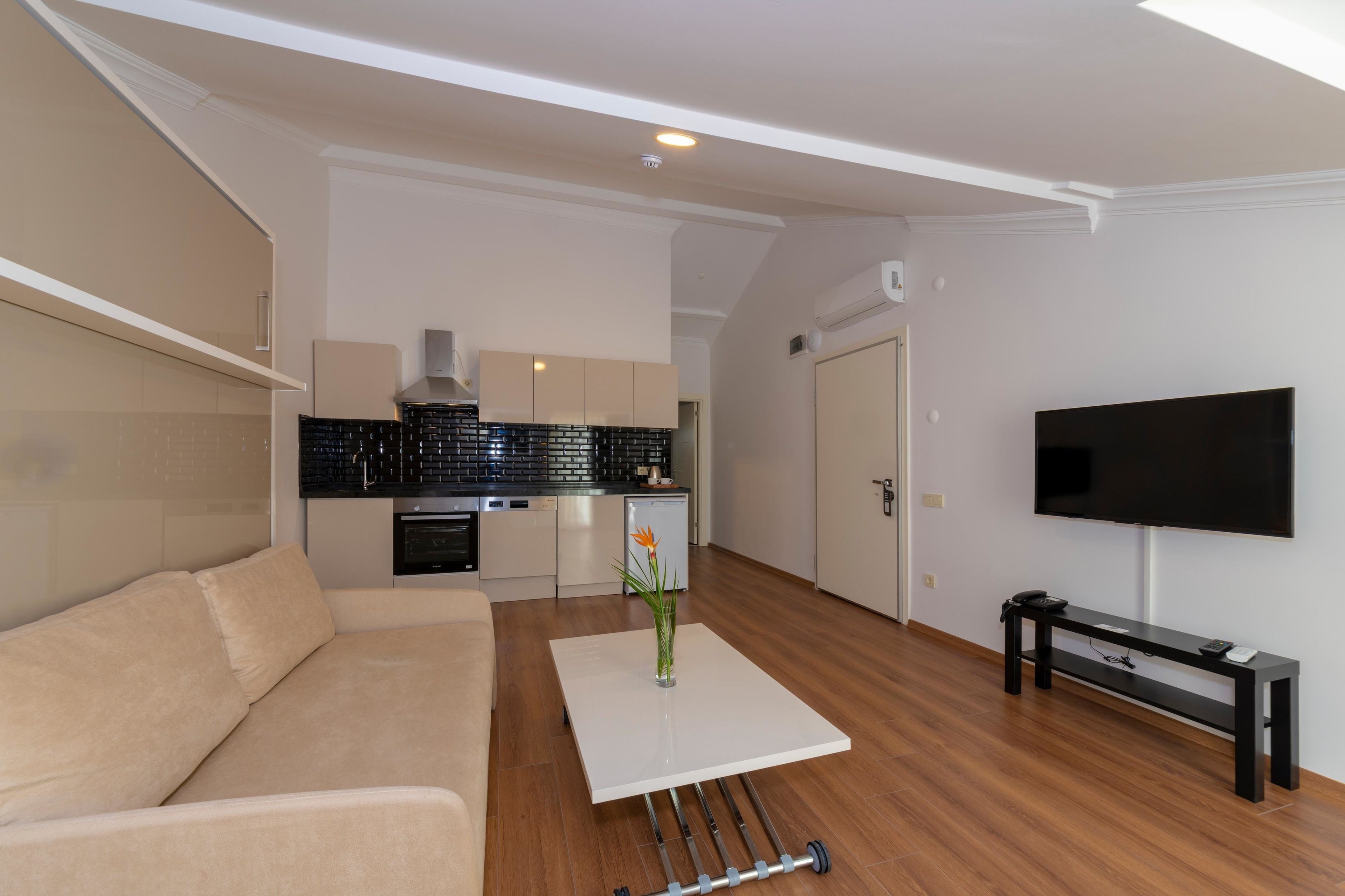 A modern living room with a sofa, a coffee table with a vase, a TV, and a kitchen in the background.