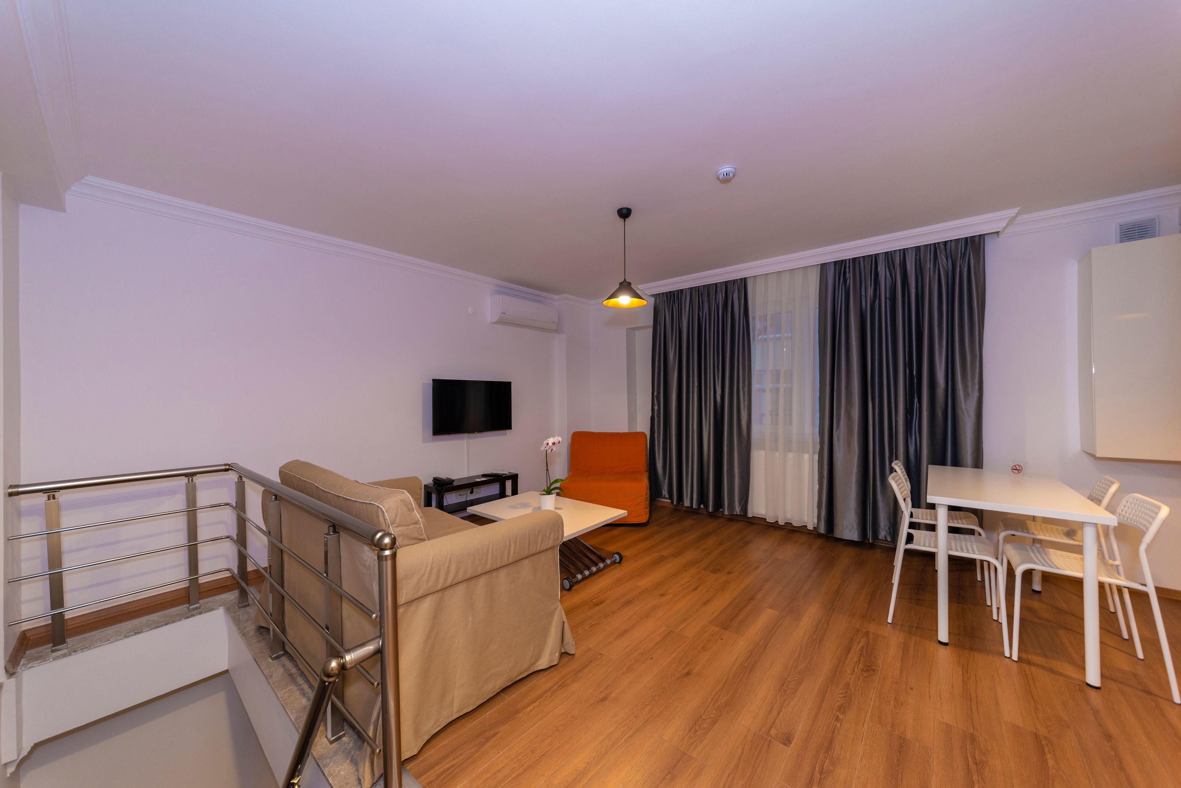 Un salon moderne comprenant un canapé, un téléviseur, une table à manger avec des chaises, un escalier et une grande fenêtre avec des rideaux.