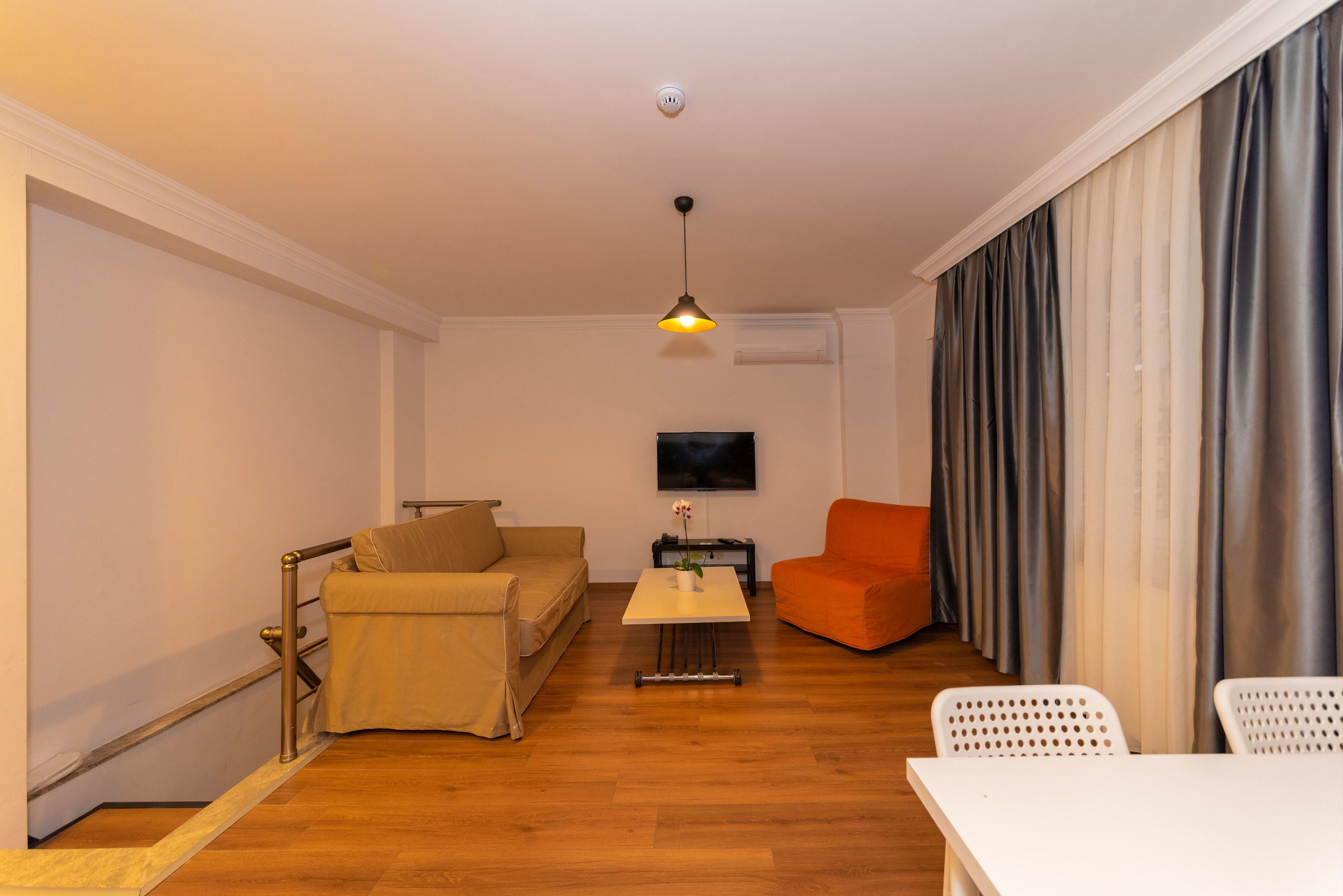 A living room with a sofa, a coffee table, an orange armchair, a TV, and a window with curtains.