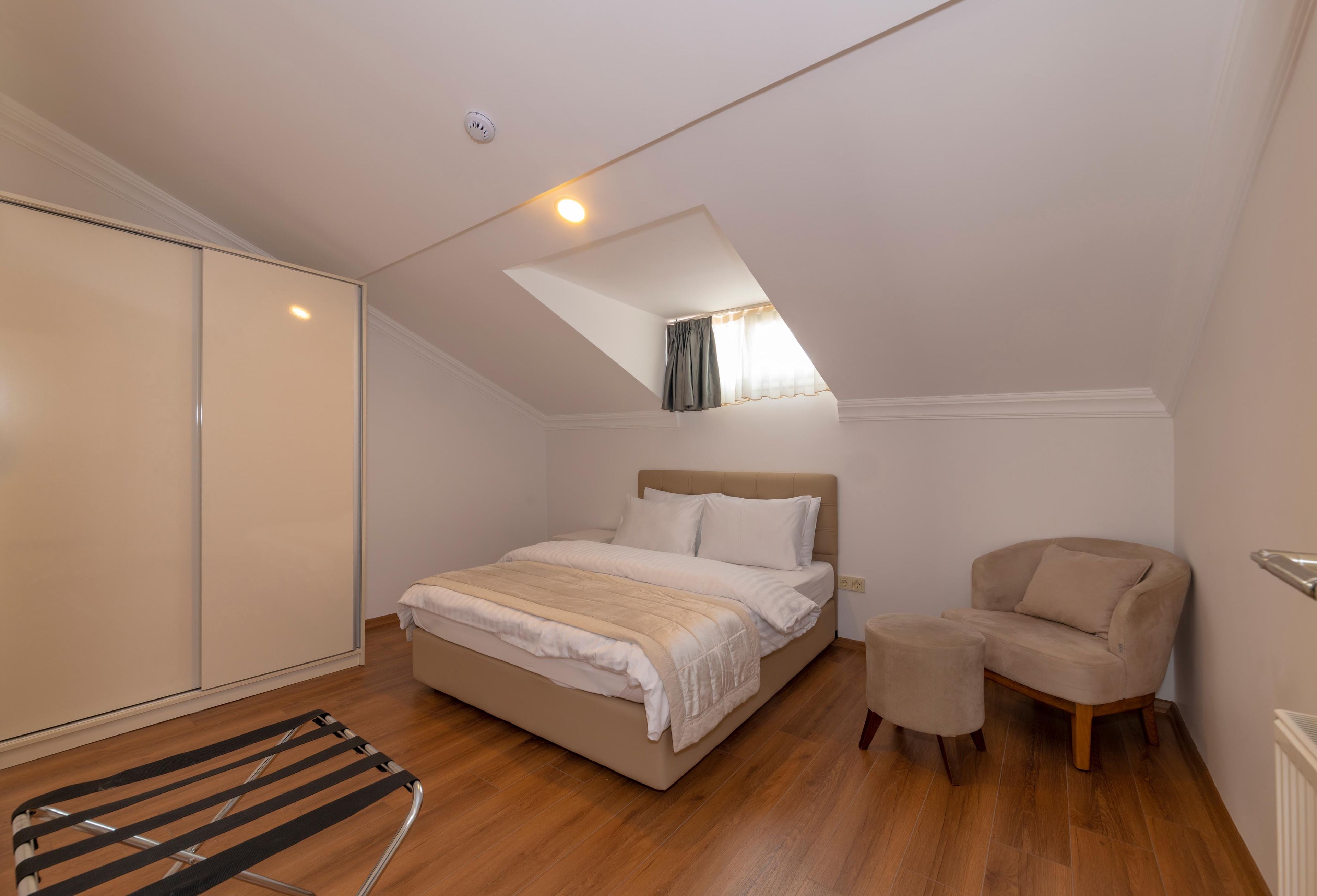 A bedroom with a bed, a chair, a small table, a radiator, and a window with curtains.