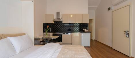 A bedroom with a bed, a kitchenette with a stove, and a door.