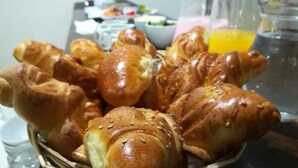 A basket of freshly baked croissants with sesame seeds, a pitcher of orange juice, and a pitcher of water on a table. - Casa Blanca Machu Picchu B&B (Machu Picchu)