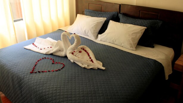 A bed with a quilted blue bedspread, two white pillows, and a heart-shaped decoration made of red roses on the bed. - Casa Blanca Machu Picchu B&B (Machu Picchu)