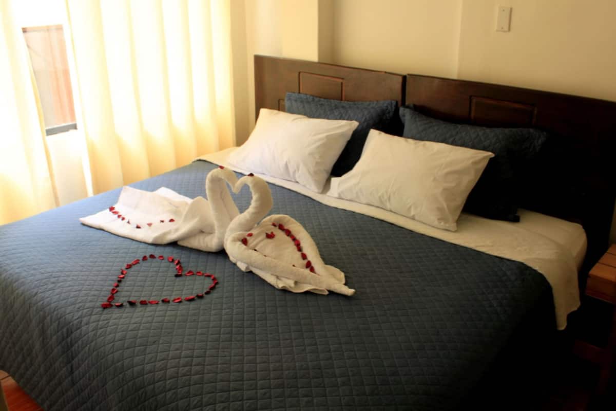 Uma cama com edredom azul acolchoado, duas almofadas brancas e uma decoração em formato de coração feita de rosas vermelhas sobre a cama.